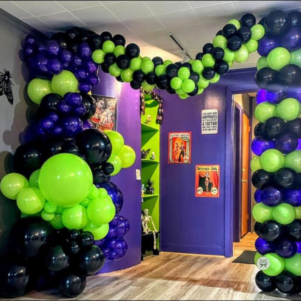 Black, neon green, and purple balloon arch framing an interior doorway in a tattoo studio, creating a bold, edgy entrance display.